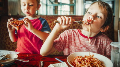 Kids' dinner time - two children eating spaghetti