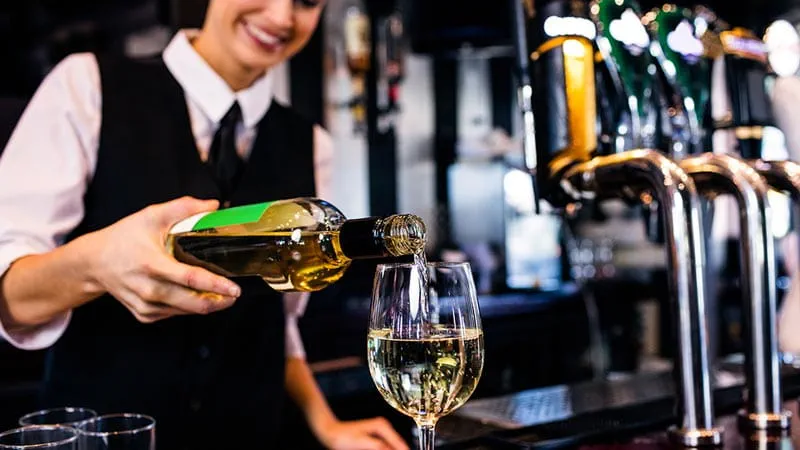 Bar – kobieta polewająca kieliszek białego wina przy barze